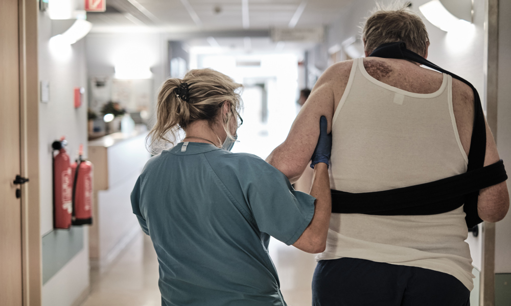 Gehversuche nach einer Fraktur: Physiotherapeutin mit einem älteren Patienten.